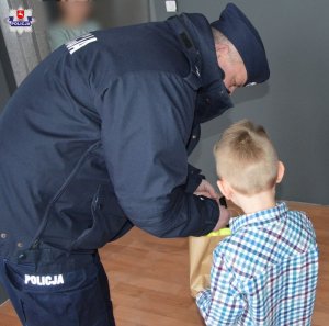 policjant wręcza chłopcu papierowa torbę z prezentami