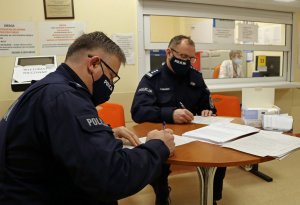 umundurowani policjanci siedzą przy stole w maseczkach, wypełniają ankiety przed szczepieniem