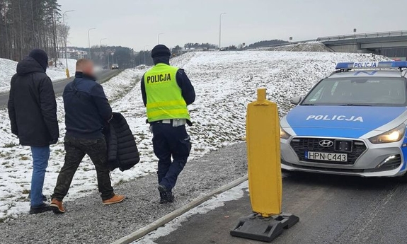 policjanci prowadzą zatrzymanego do radiowozu policyjnego