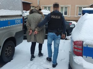 Policjant w kamizelce z napisem Policja prowadzi podejrzaną