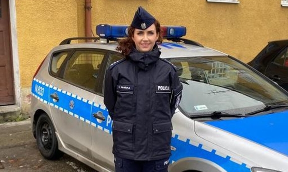 policjantka stoi przed radiowozem policyjnym, w tle budynek