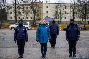 troje umundurowanych policjantów stoi na placu, miedzy nimi mężczyzna w niebieskiej kurtce