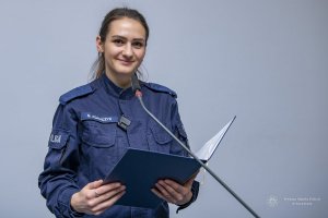 umundurowana policjantka stoi przed mikrofonem. w dłoniach trzyma otwartą teczkę