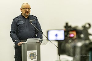 umundurowany policjant stoi za mównicą z logo Wyższej Szkoły Policji w Szczytnie