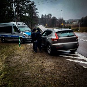 na poboczu drogi stoi brązowy samochód, obok stoi policjant a w tle radiowóz