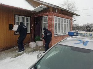 Umundurowani policjanci niosą świąteczne paczki. Po prawej stronie zdjęcia widoczny policyjny radiowóz