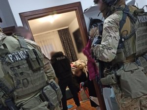 Zatrzymany mężczyzna w mieszkaniu. Policjanci stoją obok niego