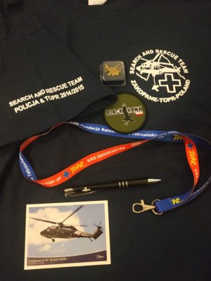 Lotnicze gadżety przekazane na licytacje, m.in.: t-shirt, podkładka pod mysz ze śmigłowcem Black Hawk, przypinka w kształcie samolotu, lotnicza naszywka z nadrukiem, zawieszka materiałowa na klucze