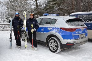 policjant i policjantka w strojach narciarskich przy oznakowanym radiowozie