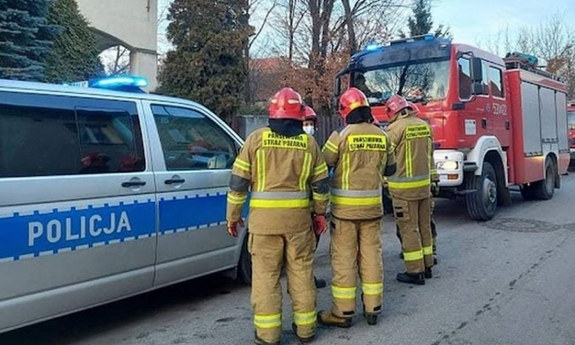 na zdjęciu widoczne są zaparkowane na ulicy pojazdy służb ratowniczych tj. straży pożarnej i policji; na ulicy stoją również strażacy
