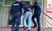 trzej policjanci prowadzą zatrzymanego mężczyznę do budynku