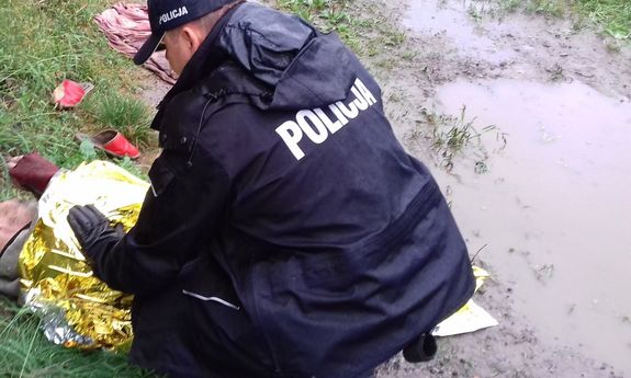 policjant podczas interwencji ratowania wychłodzonego mężczyzny. Policjant schylony okrywa mężczyznę srebrno-złotą folią