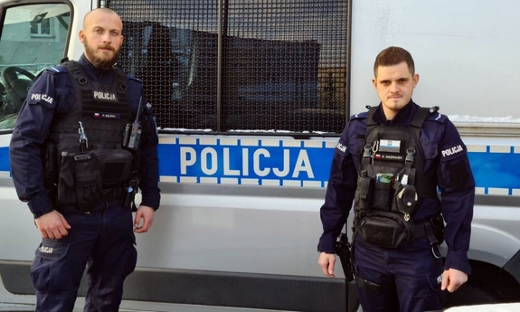 dwaj policjanci stoją przed radiowozem policyjnym