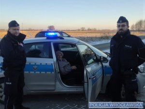 policjanci z uratowaną w lesie seniorką siedzącą w radiowozie