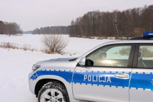 policyjny radiowóz stoi na ośnieżonej drodze przy zalewie pokrytym lodem i śniegiem