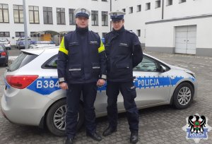 dwaj policjanci stoją przed radiowozem