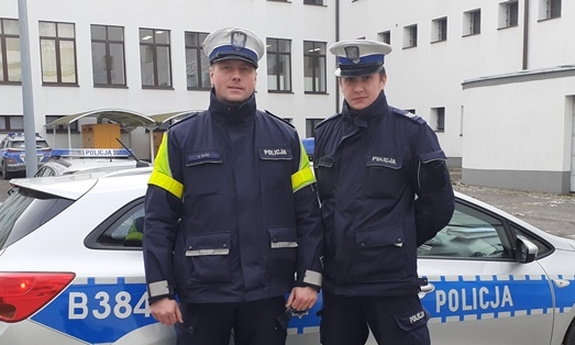 dwaj policjanci stoją przed radiowozem