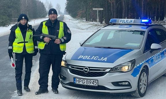 Policjantka i policjant ruchu drogowego obok radiowozu oznakowanego