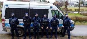 Policjanci w mundurach stoją przy radiowozie