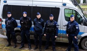 Policjanci w mundurach stoją przy radiowozie