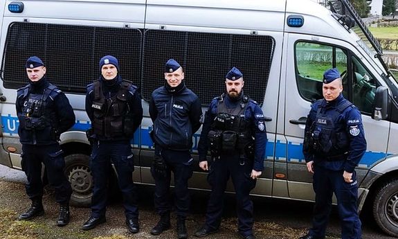 Policjanci w mundurach stoją przy radiowozie