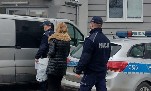 dwaj policjanci prowadzą kobietę do radiowozu