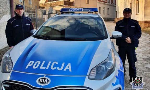 dwaj umundurowani policjanci stojący po obu stronach radiowozu