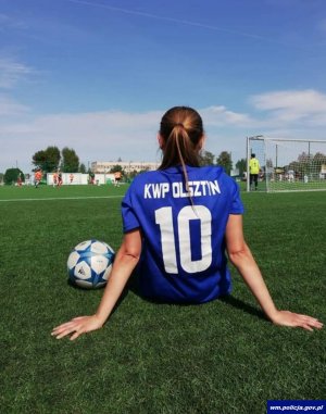 kobieta siedzi na boisku piłkarskim w koszulce drużyny, obok leży piłka