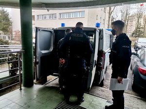 policjanci prowadzą zatrzymanego do furgonu policyjnego