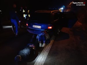 Pora nocna. Osoby zatrzymane obok pojazdu - kobieta siedzi na ziemi, mężczyzna skuty kajdankami leży na ziemi.