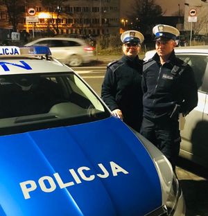 policjant i policjantka stoją przy radiowozie