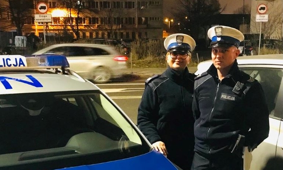 policjant i policjantka stoją przy radiowozie