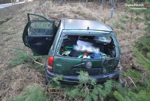 Na zdjęciu widać zniszczone auto znajdujące się w przydrożnym rowie. Samochód ma wybitą tylną szybę oraz uszkodzoną karoserię