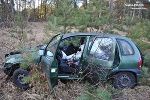 Na zdjęciu widać zniszczone auto znajdujące się w przydrożnym rowie. Samochód ma uszkodzoną karoserię, otwarte drzwi od strony kierowcy i pasażera