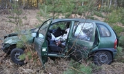Na zdjęciu widać zniszczone auto znajdujące się w przydrożnym rowie. Samochód ma uszkodzoną karoserię, otwarte drzwi od strony kierowcy i pasażera