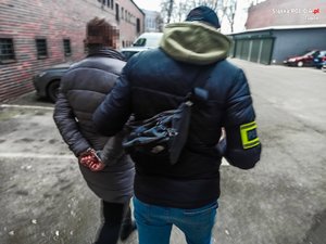 policjant prowadzi zatrzymaną kobietę na zewnątrz budynku