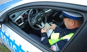 zdjęcie poglądowe, funkcjonariusz siedzący w radiowozie, policjant sprawdza dokumenty