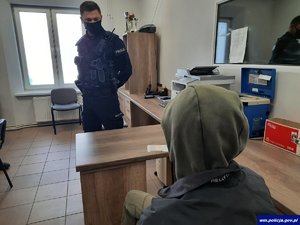 wnętrze komisariatu, policjant stoi naprzeciwko zatrzymanego siedzącego na krześle