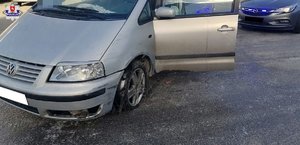 Samochód marki VW Sharan stoi na parkingu. Za nim nieoznakowany radiowóz z włączonymi światłami błyskowymi