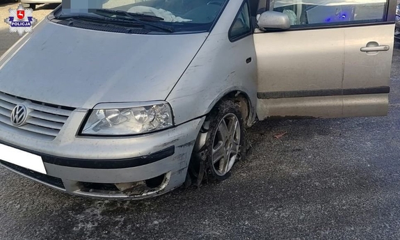 Samochód marki VW Sharan stoi na parkingu. Za nim nieoznakowany radiowóz z włączonymi światłami błyskowymi