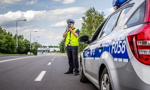 radiowóz policyjny, w tle umundurowany policjant w kamizelce odblaskowej