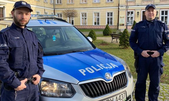 Dwaj umundurowani policjanci stoją po obu stronach radiowozu