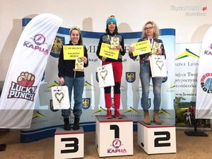 trzy kobiety stoją na podium. W środku na stopniu oznaczonym numerem jeden stoi ubrana na sportowo policjantka