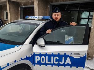 umundurowany policjant, który zatrzymał poszukiwanego w czasie wolnym od służby stoi przy oznakowanym radiowozie