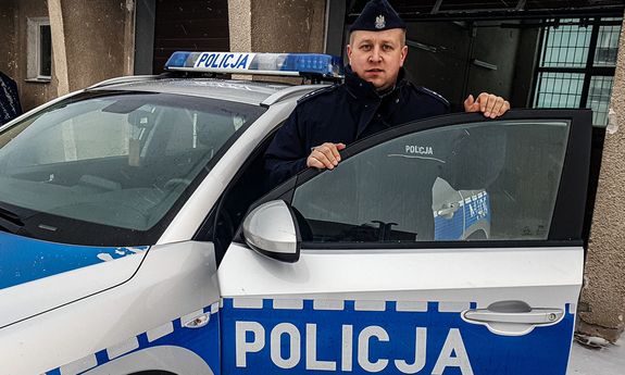 umundurowany policjant, który zatrzymał poszukiwanego w czasie wolnym od służby stoi przy oznakowanym radiowozie