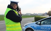policjant podczas pracy z ręcznym miernikiem prędkości, w tle oznakowany radiowóz