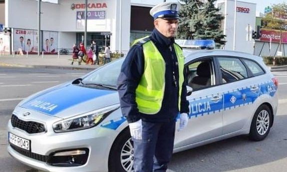 umundurowany policjant ruchu drogowego stoi przed radiowozem