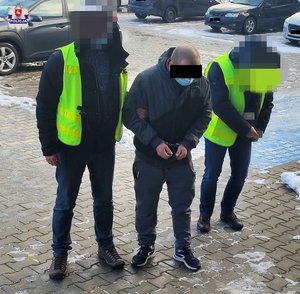 dwaj policjanci prowadzą zatrzymanego w kajdankach