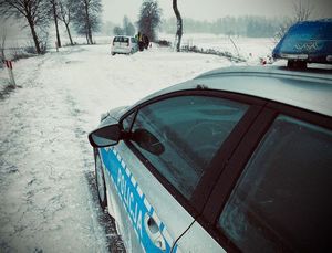radiowóz policyjny, droga zaśnieżona inne auto w zaspach i policjant