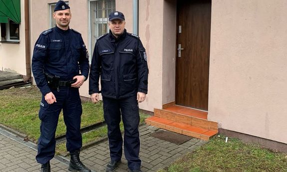 dwóch umundurowanych policjantów, który eskortowali ciężarną kobietę do szpitala stoi przed budynkiem Posterunku Policji